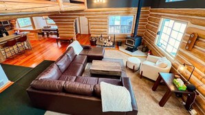 A log cabin interior with a fireplace, wooden walls, a sofa, a dining area, and a kitchen.