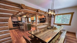A rustic kitchen with wooden beams, a long wooden table, and a large window.