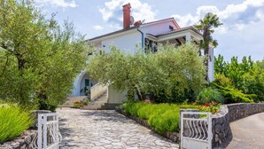 Una casa con un sendero de piedra que conduce a una entrada blanca, rodeada de abundante vegetación y un cielo despejado.
