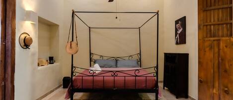 A four-poster bed with a red bedspread, a ceiling fan, a wall-mounted lamp, and a wooden door.