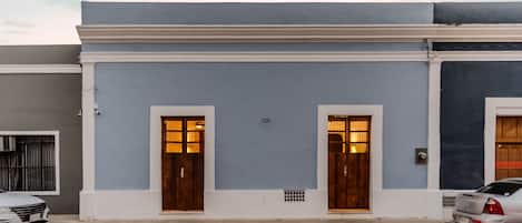 Un bâtiment à deux étages, doté d’une façade bleue et de bordures blanches. Il y a deux portes en bois avec des panneaux de verre, et une petite fenêtre au rez-de-chaussée.
