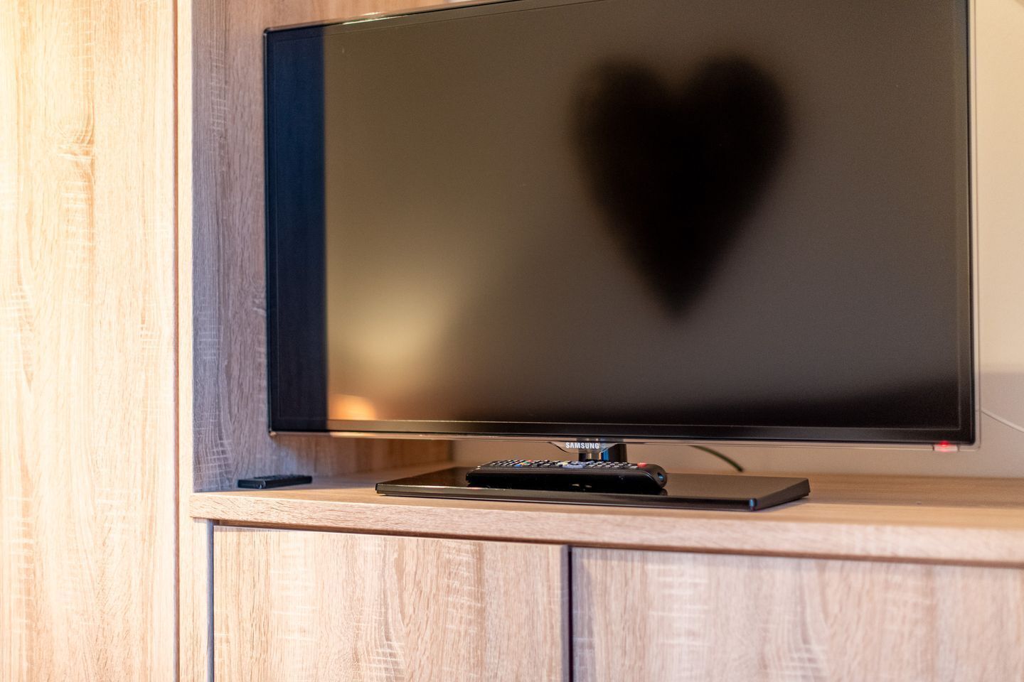 A flat-screen TV mounted on a wooden cabinet with a remote control on a stand below it.
