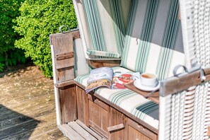 A wooden bench with a striped cushion and a magazine, a cup of coffee, and a wicker chair. - Wohnung Elfzwei - Strandnah. Modern. Zentral (Sylt)