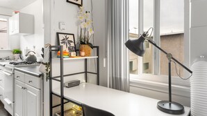 A modern kitchen with white cabinets, a stove, and a sink. There is a desk with a lamp and a potted plant.