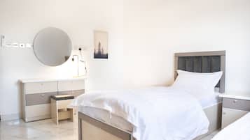 A modern bedroom with a large bed, bedside tables, a dresser, a round mirror, and a wall-mounted lamp.