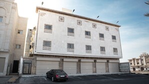 A multi-story building with a flat facade, multiple windows, and a car parked in front.