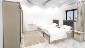 A modern bedroom with two beds, a small table, and a window with a view.