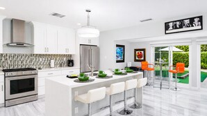 Una cocina moderna con una isla central, electrodomésticos de acero inoxidable y un comedor con taburetes de bar.