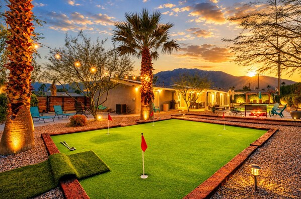 Un campo da golf con un putting green, palme e un edificio con posti a sedere all'aperto.