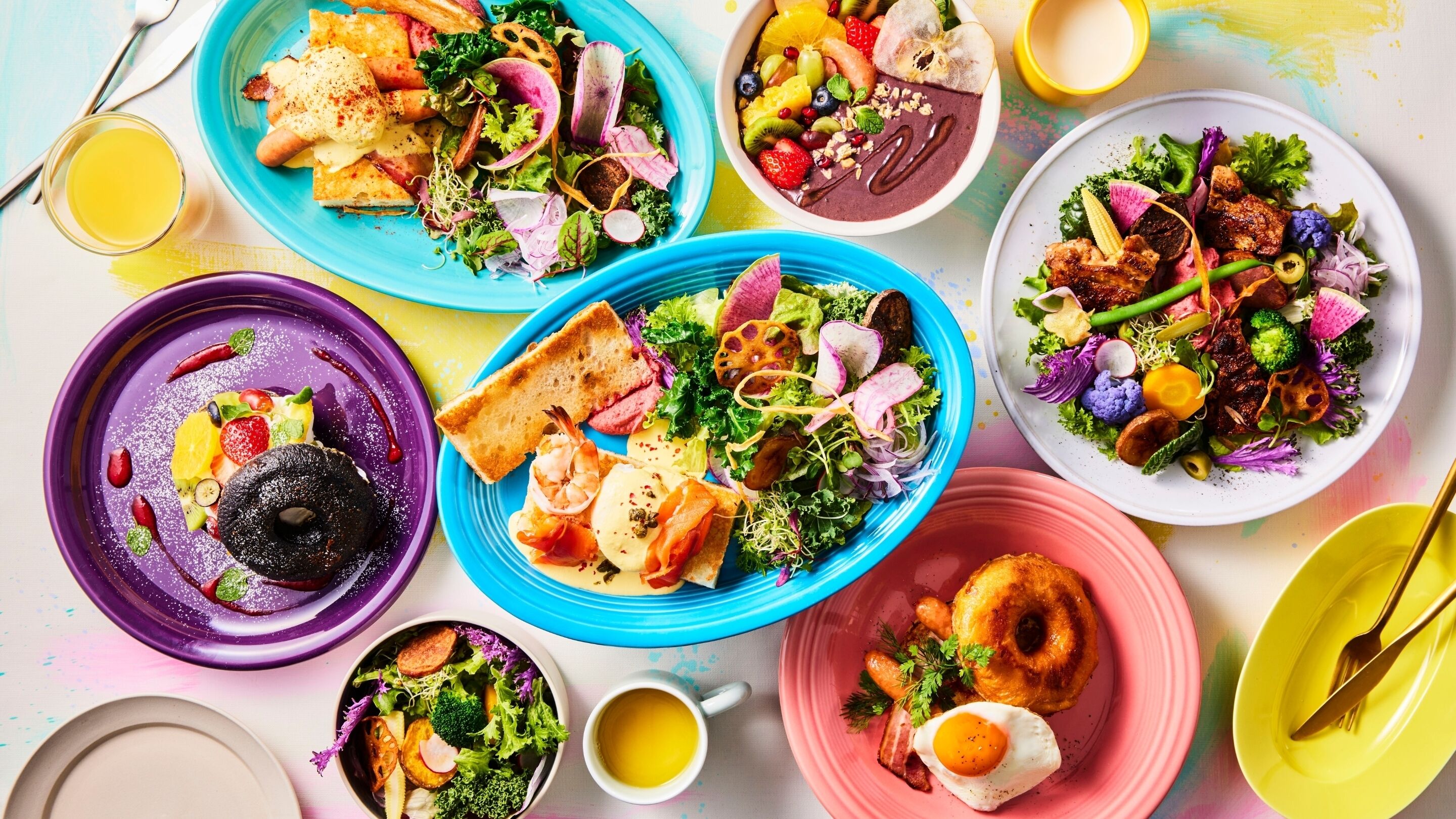 A variety of colorful dishes on a table, including salads, fruits, and a cup of coffee.