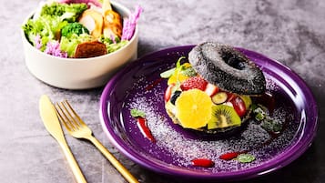 A purple plate with a dessert topped with a chocolate ring, surrounded by fruits and garnished with mint leaves.