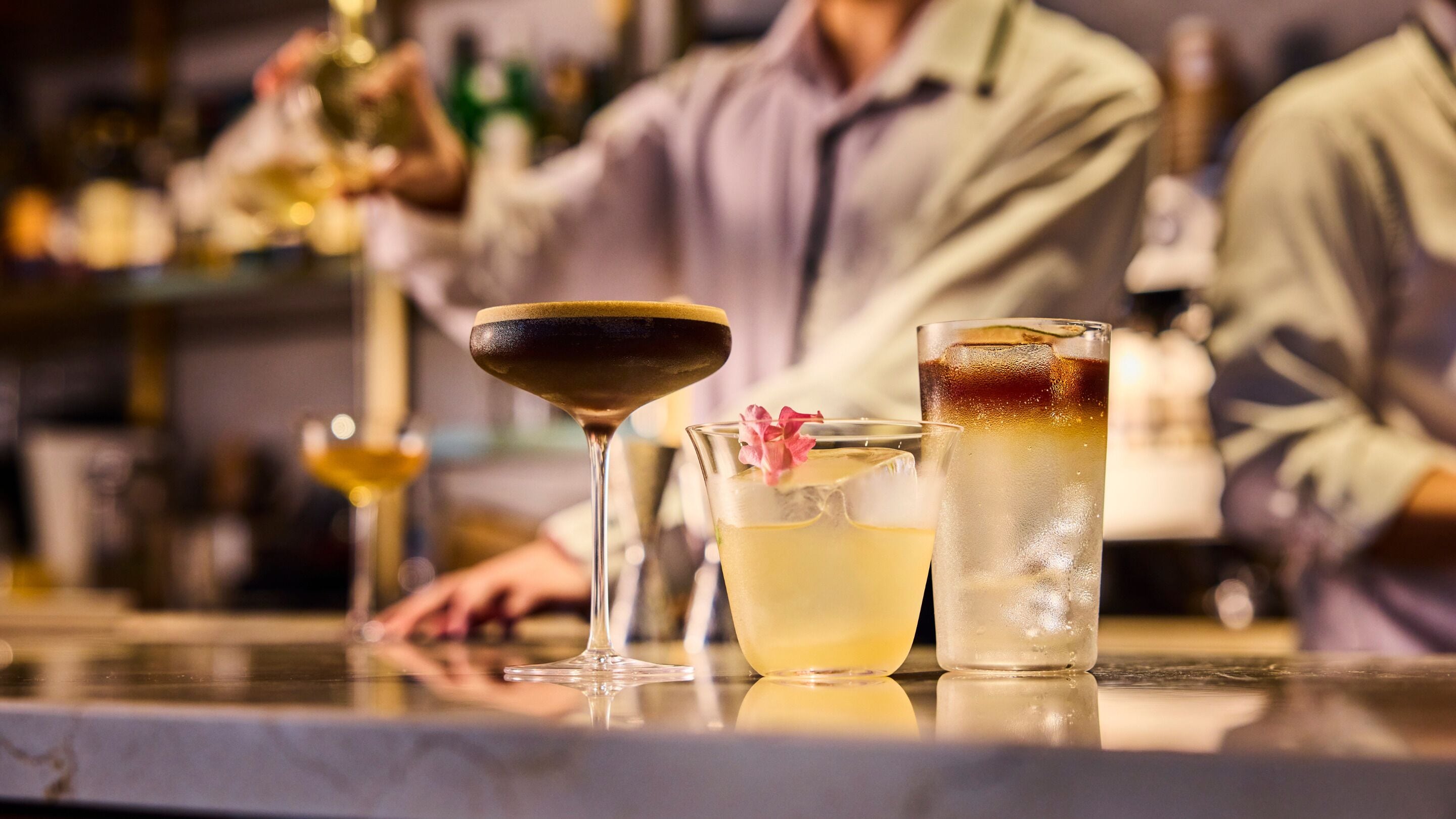 En bar med forskellige drikkevarer, heriblandt en martini, en cocktail med blomsterpynt og en sodavand med is.