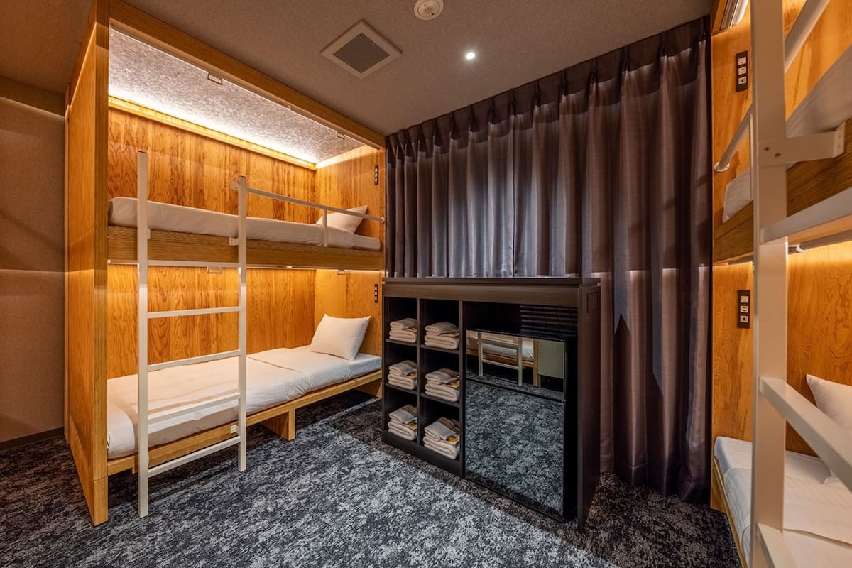 A compact, well-lit room with bunk beds, a small desk, and a wardrobe with shelves.