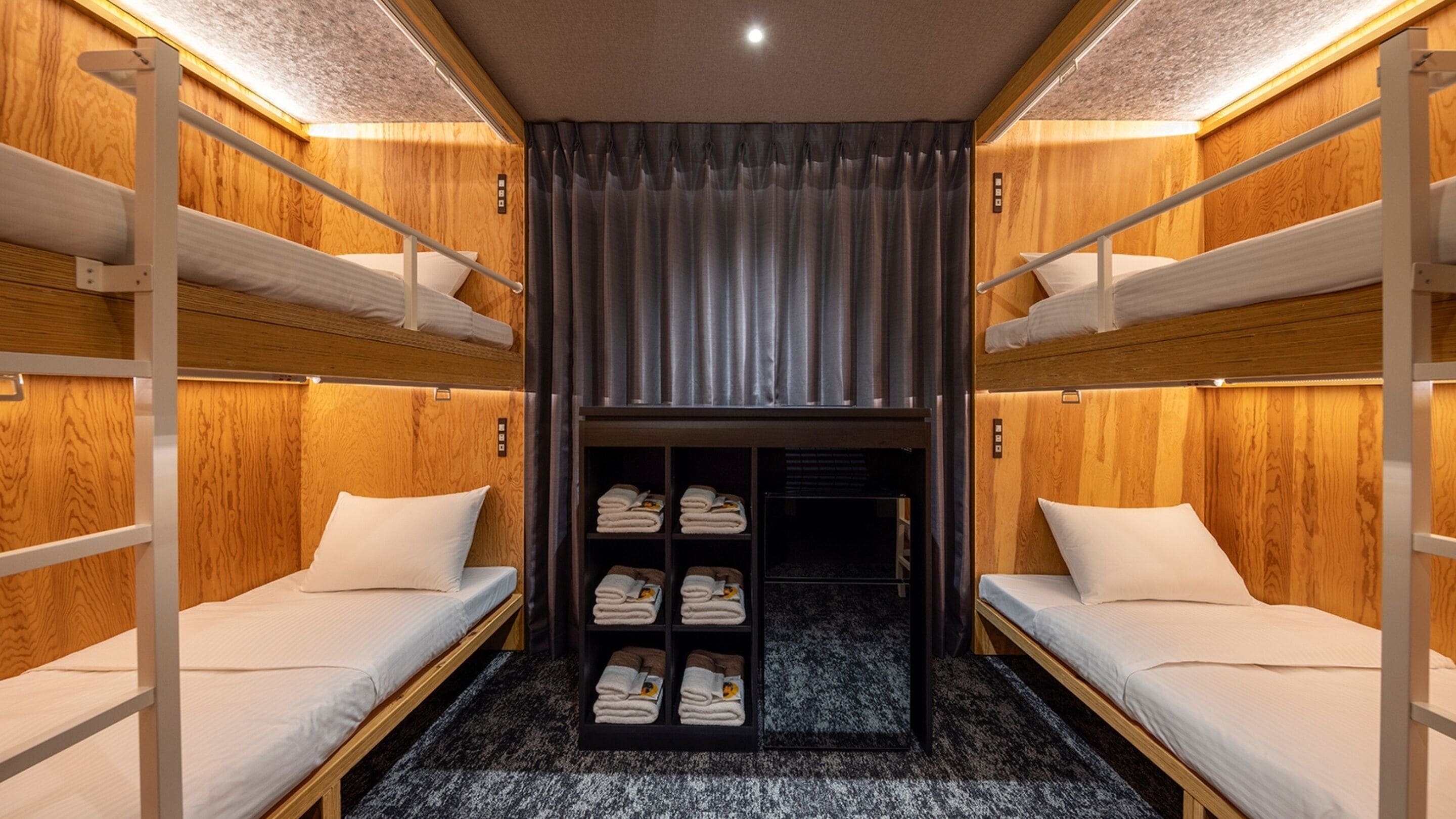 A bunk bed room with wooden walls, a central closet with shelves, and a ceiling light.
