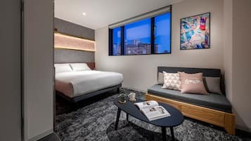 Una habitación de hotel moderna con cama, sofá, mesa de centro y ventana con vista a la ciudad.