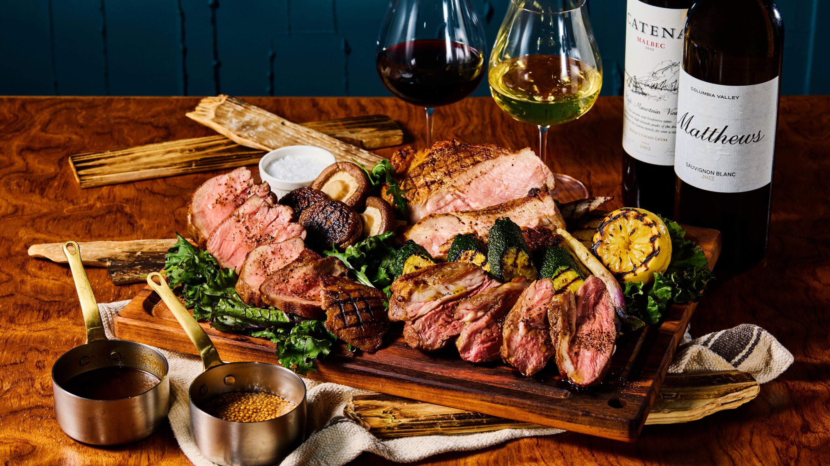 Ein Holzschnittbrett mit geschnittenem Fleisch, Gemüse und einer Weinflasche.