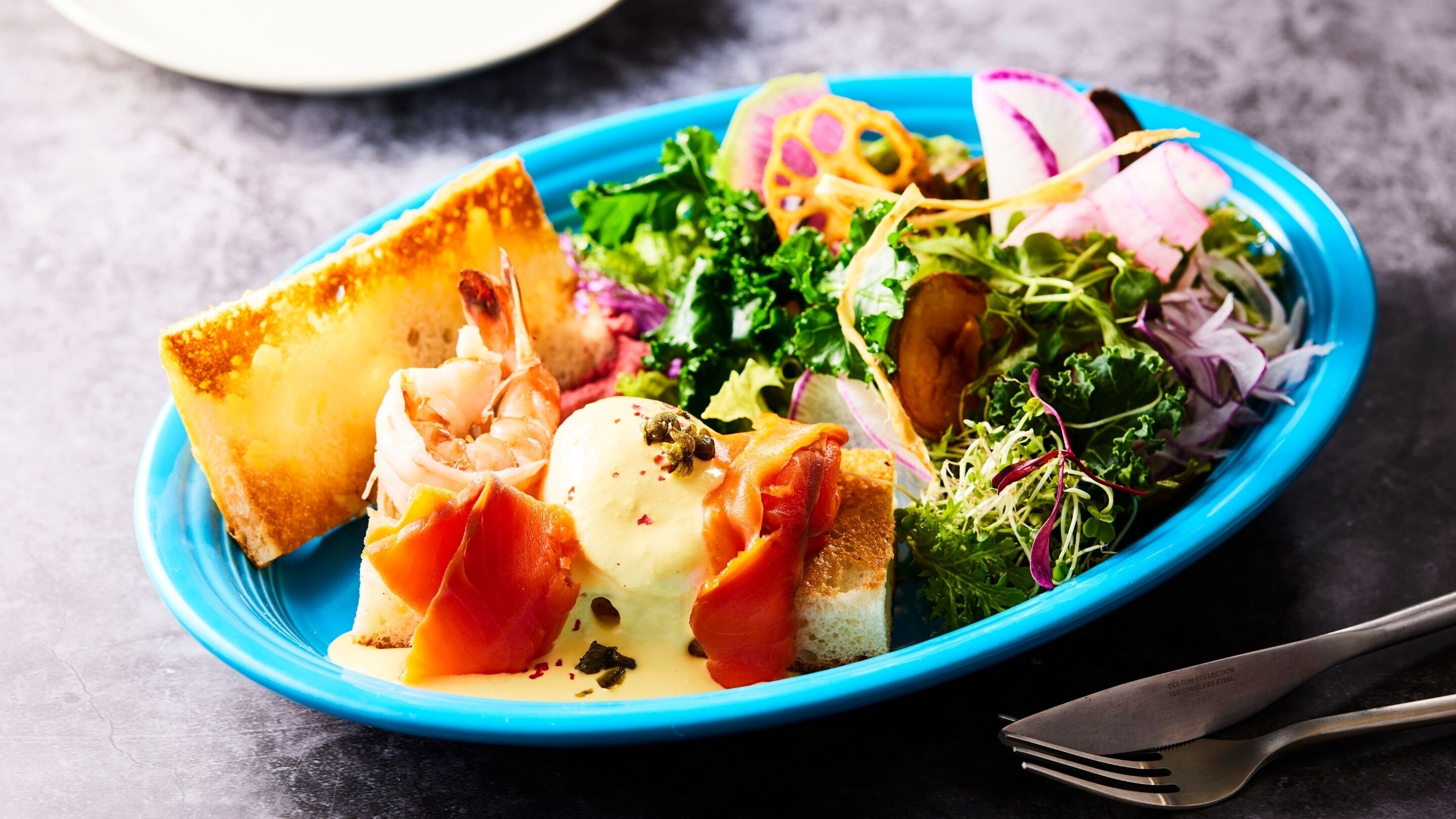 A blue plate with a salad, bread, and shrimp.