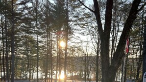 Deux fauteuils Adirondack avec des couvertures, un barbecue et une vue sur les arbres et le coucher de soleil.