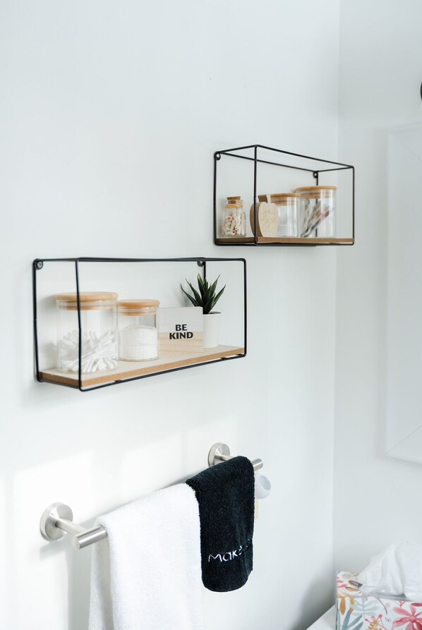 A bathroom with two wall-mounted shelves, one holding jars and a plant, and the other with a towel rack and a towel. - Riverside Blue… Your cozy guesthouse for all things Muskoka.!! (Bracebridge)