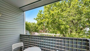 A balcony with a white table and two chairs, a metal fence, and trees in the background. - I18 - Apt|Yard|11mi to Fair Park|Sleeps 4 (Irving)