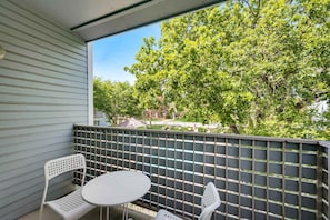 A balcony with a white table and two chairs, a metal fence, and trees in the background. - I18 - Apt|Yard|11mi to Fair Park|Sleeps 4 (Irving)