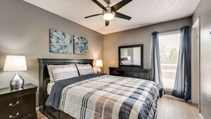A bedroom with a bed, bedside tables, a ceiling fan, artwork, a mirror, and a window with curtains. - I18 - Apt|Yard|11mi to Fair Park|Sleeps 4 (Irving)