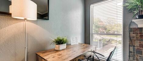 Een modern interieur met een houten bureau, een zwarte stoel, een vloerlamp en een raam met jaloezieën.