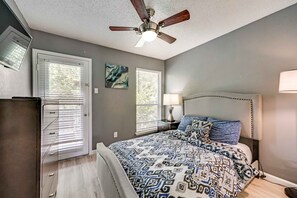 A bedroom with a bed, a ceiling fan, a nightstand, a lamp, and a window with blinds.