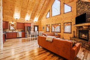 Interior de una cabaña de troncos con comedor, cocina, sala de estar y chimenea.