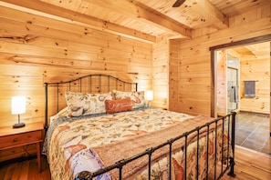 A wooden cabin bedroom with a bed, nightstands, and a door leading to another room.