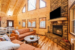 A cozy log cabin interior with a fireplace, wooden walls, and a sofa.