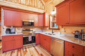 Una cocina con paredes de madera, armarios rojos, electrodomésticos de acero inoxidable y encimera de granito.
