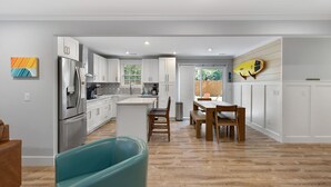 A modern kitchen with white cabinets, stainless steel appliances, and a dining area with wooden furniture.