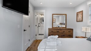 A hotel room with a bed, a wooden dresser, a mirror, a flat-screen TV mounted on the wall, and a window with a view.