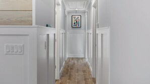 A narrow hallway with white walls, a wooden floor, and a framed artwork on the wall.