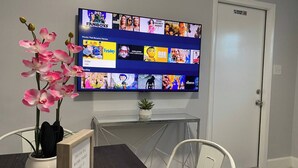 Huoneessa on seinälle asennettu televisio, jossa näkyy elokuvavalikoima. Pöydällä on ruukkuorkidea, seinällä kehystetty inspiroiva sitaatti ja sivupöydällä pieni kasvi.