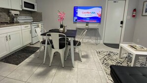 Moderni keittiö, jossa on valkoiset kaapit, mikroaaltouuni ja kahvinkeitin. Keittiössä on myös ruokailutila, jossa on pöytä, tuolit ja televisio, jolla näkyy kanava nimeltä ’CashNetUSA  ’.