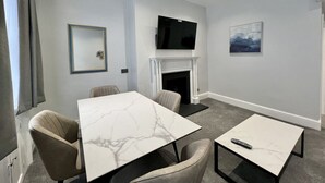 Una habitación de hotel moderna con una mesa de comedor de mármol, asientos cómodos, un televisor de pantalla plana, chimenea y obras de arte en las paredes.