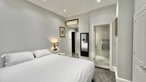 Habitación de hotel con una cama grande, mesitas de noche, un espejo y zona de ducha.