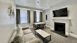 Una sala moderna con un sofá, una mesa de centro, una mesa de comedor con sillas, una chimenea y un televisor montado arriba.