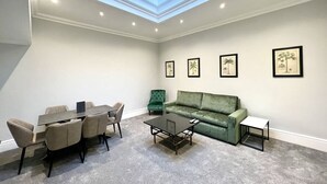 Ein Konferenzraum mit hoher Decke, einem Oberlicht, einem grünen Sofa, einem Couchtisch und einem Esstisch mit Stühlen.