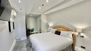 Ein modernes Hotelzimmer mit einem großen Bett, einem flachbildfernseher an der Wand und einer kleinen Sitzecke mit einem Sessel.