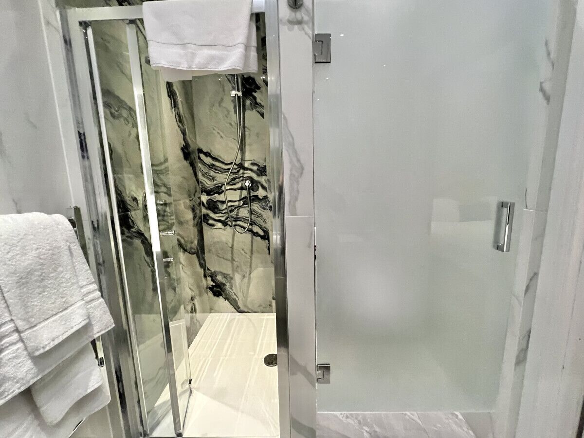 A modern bathroom with a glass shower enclosure, marble wall, and a white towel on the floor.