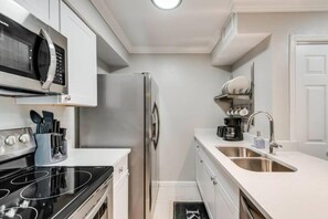 A modern kitchen with a black stove, stainless steel refrigerator, white cabinets, and a double sink. - I32 - Apt|Patio|11mi to Convention Ctr|Sleeps 2 (Irving)
