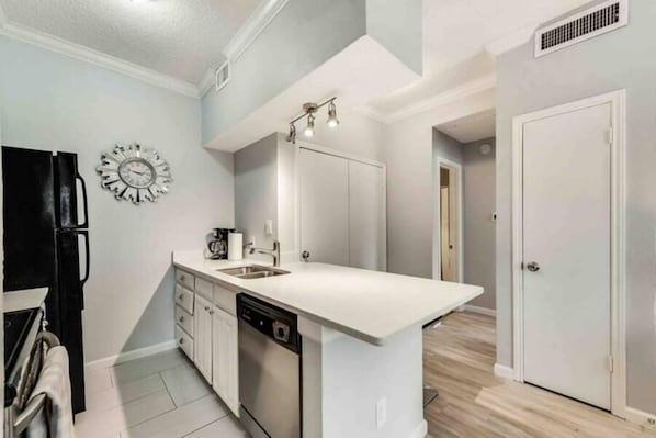 A modern kitchen with a dishwasher, a sink, and a clock on the wall.