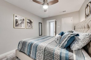 A bedroom with a bed, a ceiling fan, and two framed pictures on the wall.