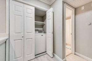 A laundry room with a washing machine and dryer, a white door, and a hallway leading to another room. - I32 - Apt|Patio|11mi to Convention Ctr|Sleeps 2 (Irving)