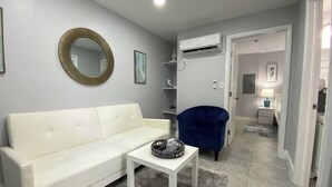 Un salón con un sofá blanco, un sillón azul, un espejo redondo y una mesita con un objeto decorativo.