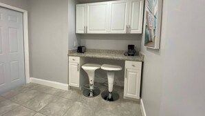 Cocina compacta con armarios blancos, encimera de granito y cafetera.