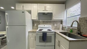 Una cocina con armarios blancos, estufa, lavabo y refrigerador.